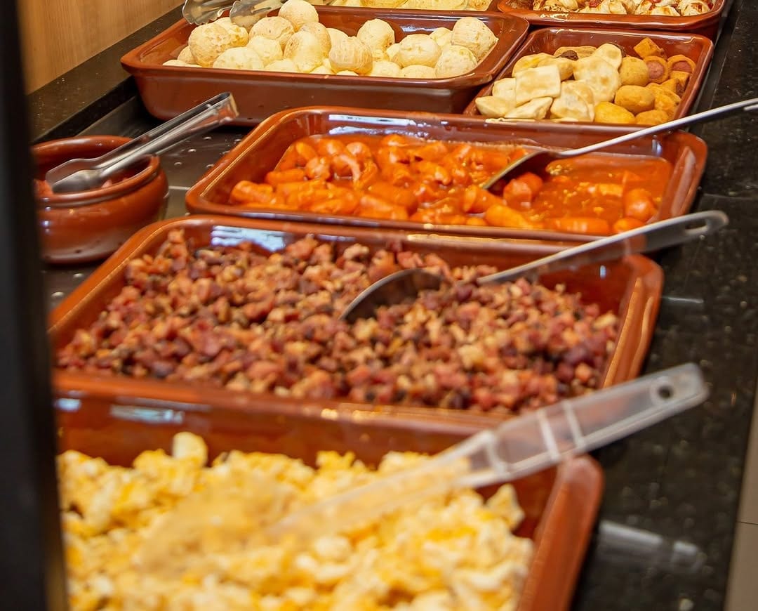 Travessas de ovos mexidos, linguiça e quitutes no buffet do café colonial